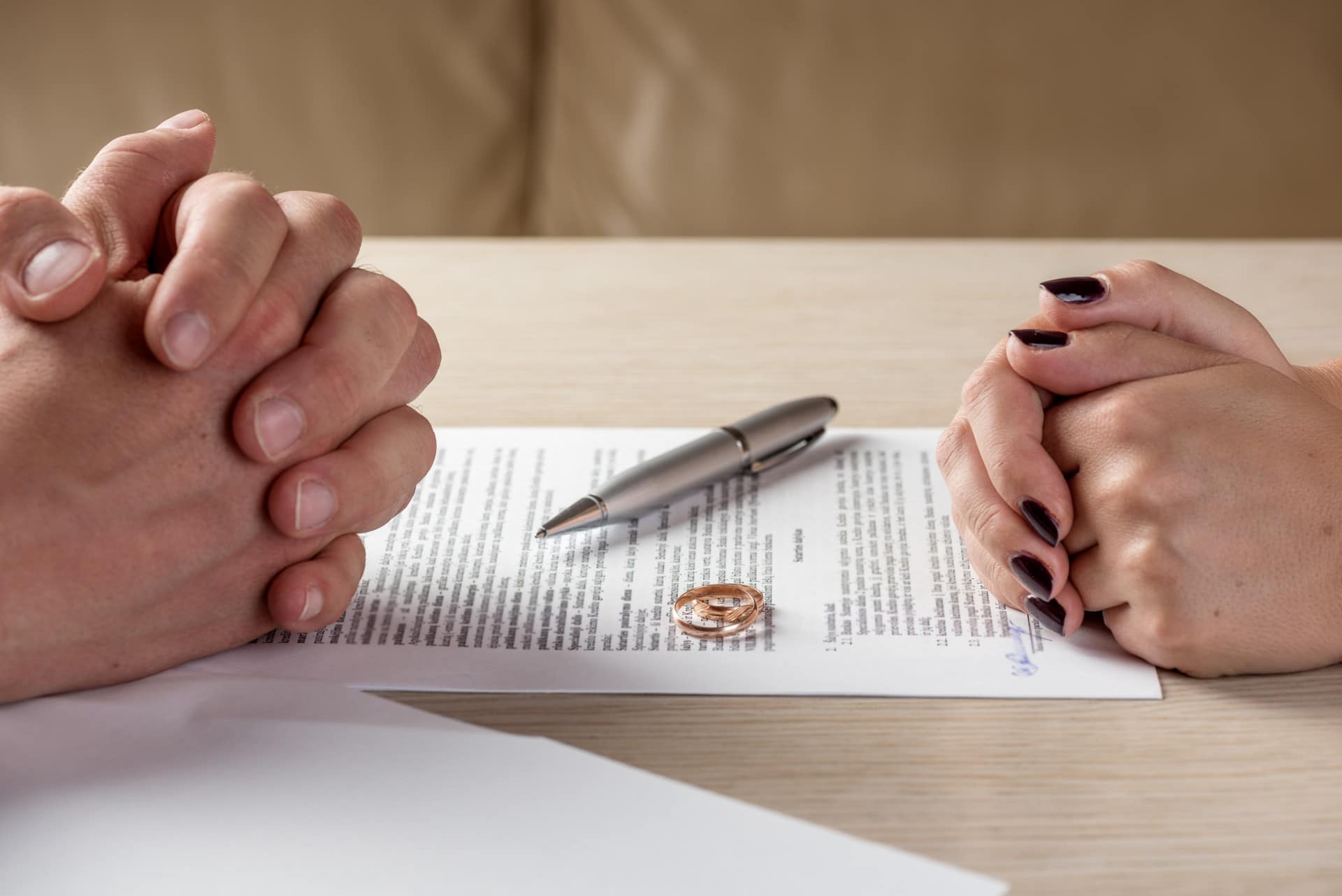 a couples hands across form each other with their rings on top of their divorce papers